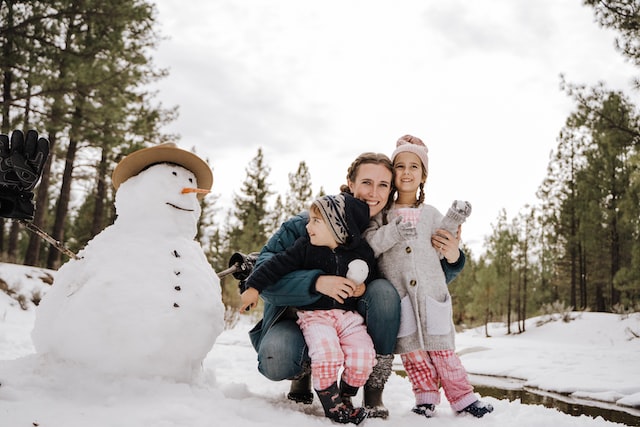 a women and two children outside next to a snowman